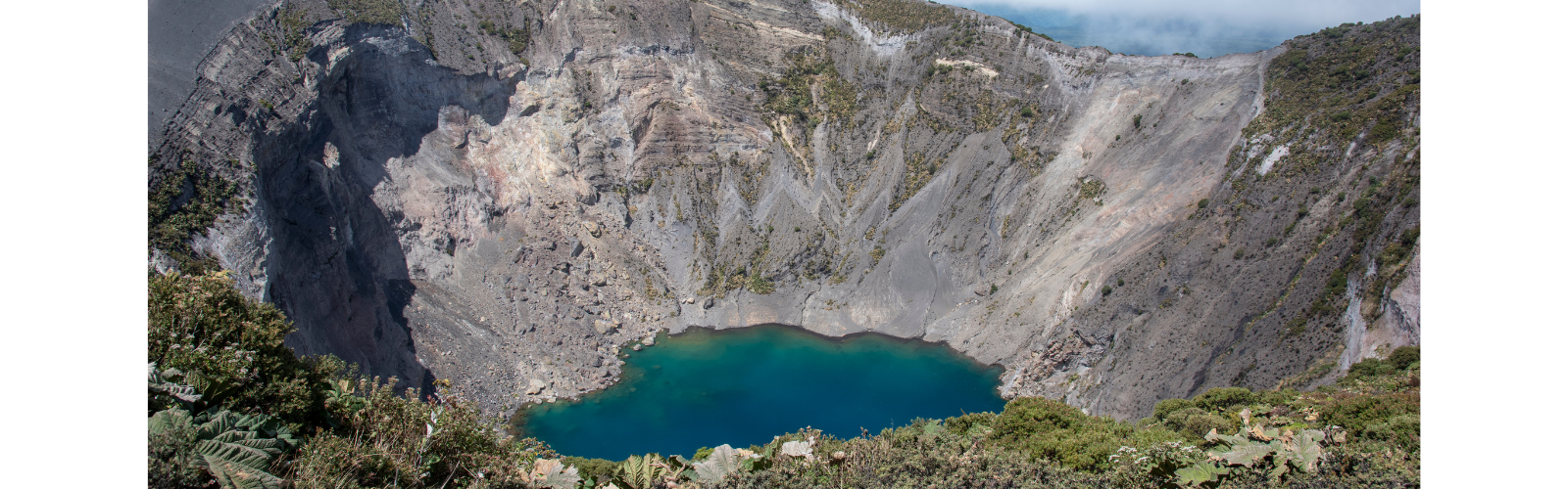 Drone shot of an oasis in the middle of a crater. Fog is surrounding the crater in the background.